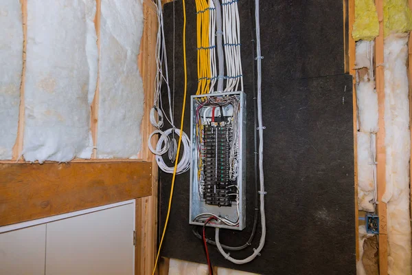 Electrical panel in a partially finished room with exposed insulation. Multiple wires are connected, and some loops are visible.